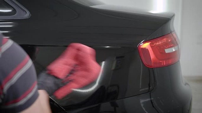 师傅在汽车车间用红色软布清洗后抛光汽车后部