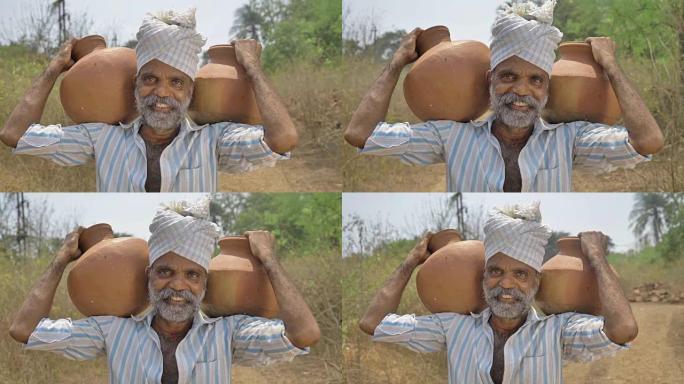一个快乐而微笑的男性农民在乡下肩上扛着两个装满淡水的土锅。