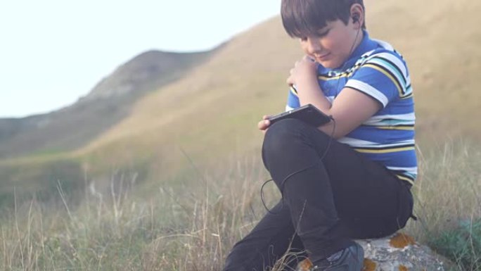 一个男孩坐在大自然的一块岩石上使用手机