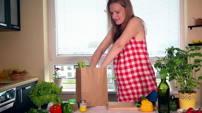 微笑的怀孕妻子在厨房里卸下装有有机蔬菜的购物袋