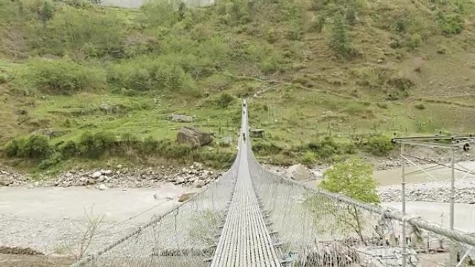 背包客在尼泊尔河上的吊桥上行走。马纳斯鲁巡回赛。
