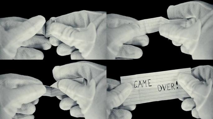 一个戴着手套的人在一张纸上展开一张纸条，上面写着: 游戏结束