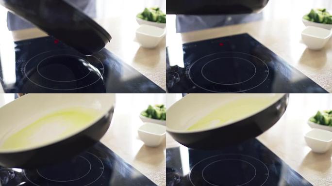 男子在厨房慢动作的电磁炉上在锅上撒上橄榄油