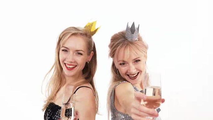 2个美丽开朗的双胞胎女孩，戴着一杯香槟，在白色背景的工作室里摆姿势
