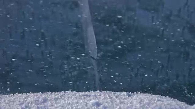 雪在冰面上飞舞。雪花在贝加尔湖的冰上飞舞。冰非常美丽，有不同寻常的独特裂缝。雪闪闪发光，发出红色光芒