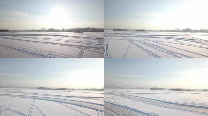 日落时分，汽车在雪湖上弯曲的冰道上行驶。鸟瞰图。一辆汽车驶过乡村公路上的冬季森林。无人机的俯视图