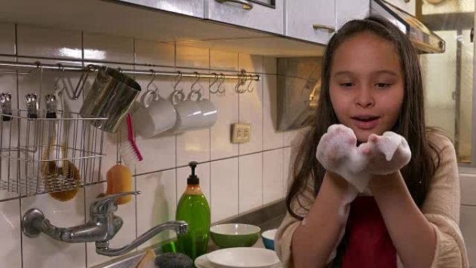 Tween亚裔美国女孩洗碗，手套上吹泡沫