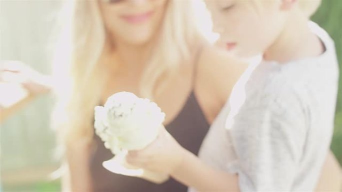 年轻慈爱的母亲抱着她的孩子，给她的儿子一个冰淇淋蛋卷，他开始在公园吃。