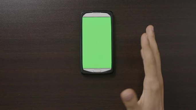 千禧一代男子的俯视图在绿屏智能手机前做手势，用拇指竖起OK心脏手指手势评估应用程序