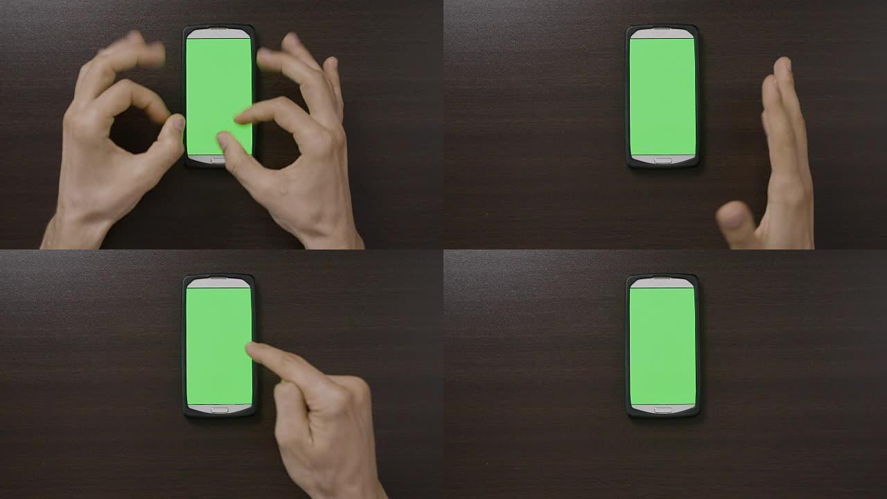 千禧一代男子的俯视图在绿屏智能手机前做手势，用拇指竖起OK心脏手指手势评估应用程序