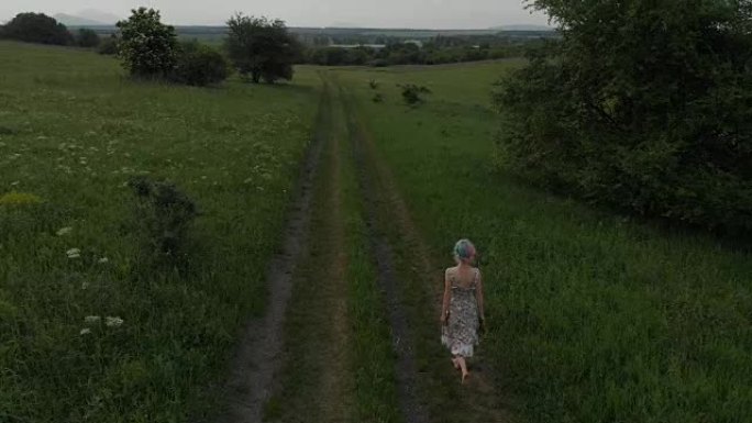 开朗的年轻女孩赤脚走在乡间小路上。鸟瞰图。拍摄于马维克航空4k 100kbps