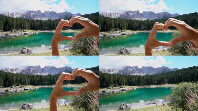 特写女性的手在美丽的高山湖上制作心形手指框