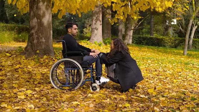 在秋季公园与女友坐在轮椅上的残疾男子