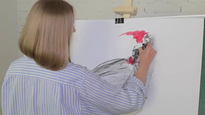 金发女艺术家用煤在画布上画一个女人。画布立在画架上。绘图过程