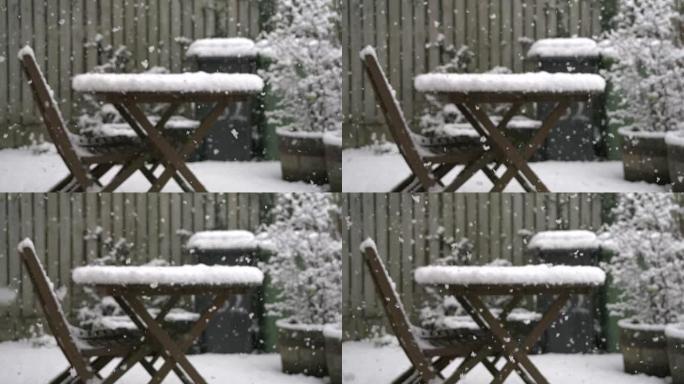 雪落在带有家具和带轮垃圾箱的英国花园里
