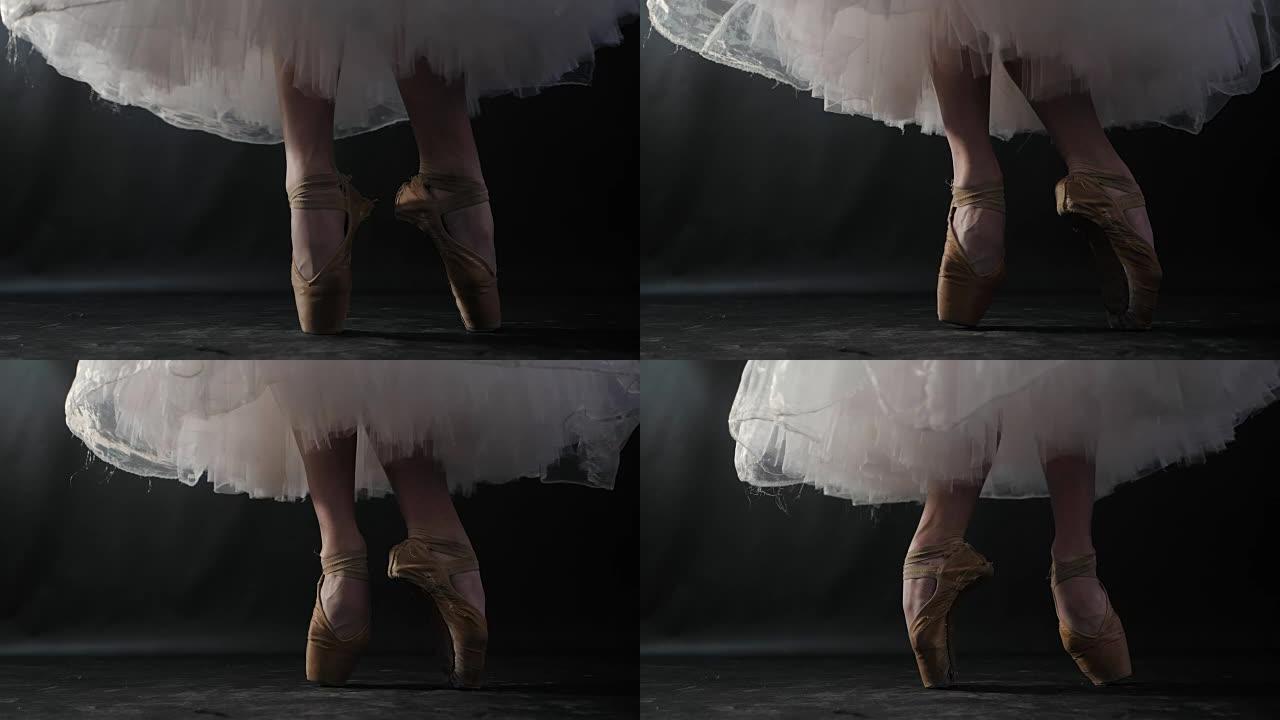 芭蕾舞演员在黑暗的舞台或工作室练习时的特写镜头。穿着尖头鞋的女人的脚。芭蕾舞女演员展示经典芭蕾舞剧。