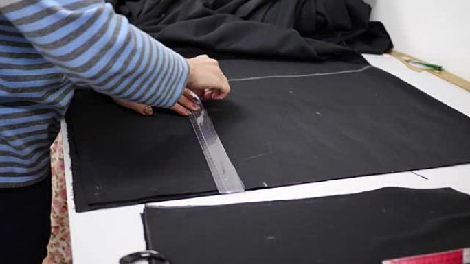 带粉笔和尺子的裁缝师在工作室里测量桌子上的布料