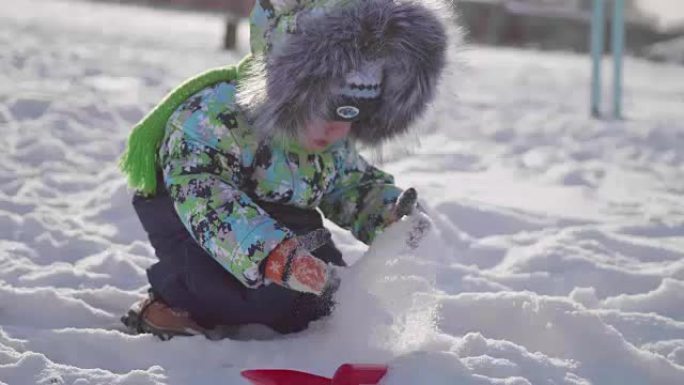 一个在冬季公园玩雪的小孩。阳光明媚的冬日。新鲜空气中的乐趣和游戏。