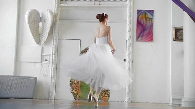 穿着白色连衣裙的年轻漂亮芭蕾舞演员在宽敞的白色工作室表演舞蹈