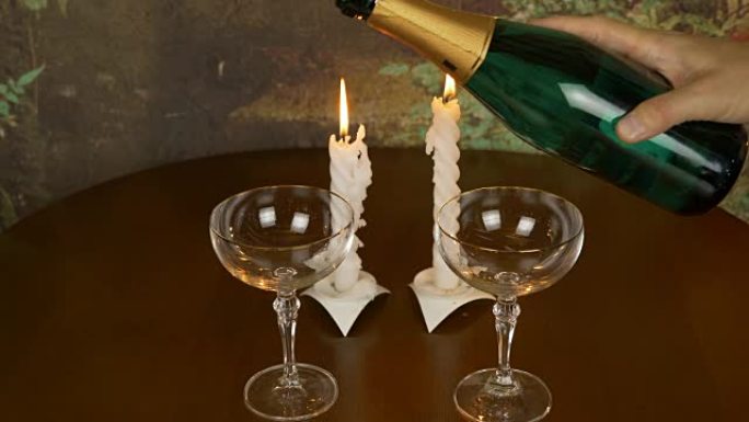 浪漫夜晚的开始。桌子上有两个酒杯和一瓶香槟。男人的手把香槟倒在玻璃杯上。用打火机的手点燃蜡烛。