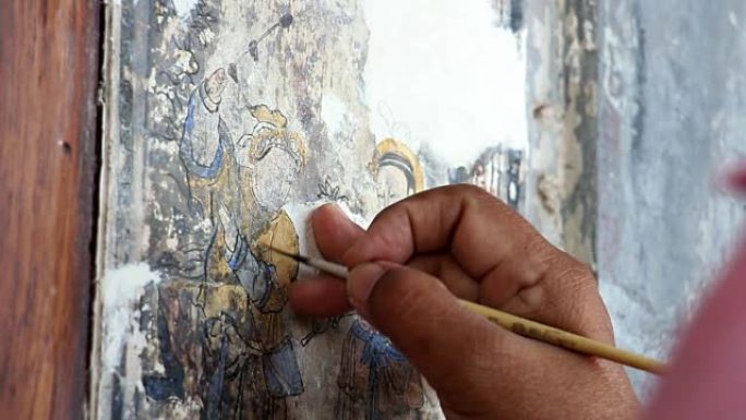 一位绘画艺术家的手正在修复一幅中国画。旧建筑墙壁上的中国画翻新。