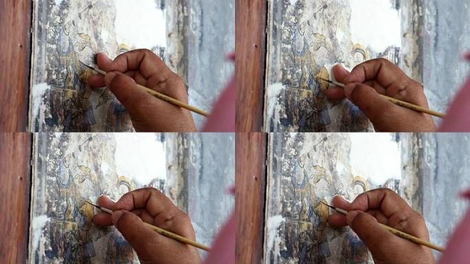 一位绘画艺术家的手正在修复一幅中国画。旧建筑墙壁上的中国画翻新。