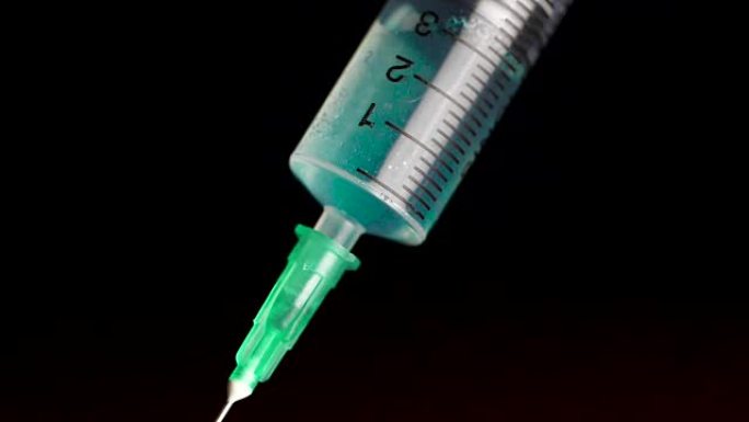 将疫苗从黑色背景上的安瓿放入玻璃注射器中。特写。注射器是从疾病严重疾病中注射绿松石液，医学的概念