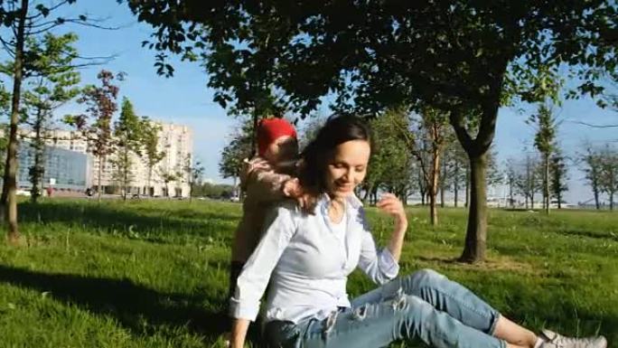 年轻的母亲在公园里和她的孩子玩耍。幸福的女人穿上孩子的背