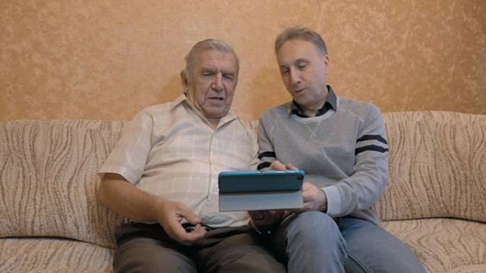 老人和他成年的儿子，看看平板电脑。儿子教父亲使用现代技术。