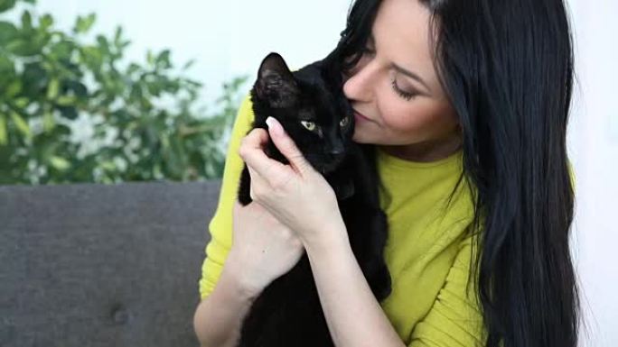 对宠物的爱。美丽的黑发女孩和一只黑猫正在沙发上的客厅里放松。