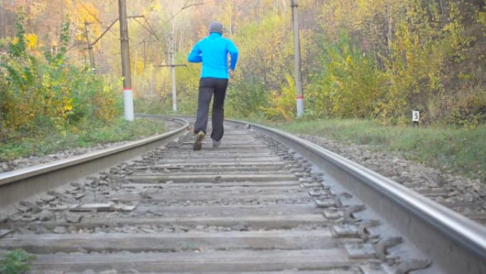 男子慢跑火车在秋天的森林里追踪铁路。在鼓舞人心的秋季景观中越野跑步时，在户外训练和锻炼。运动动机。慢