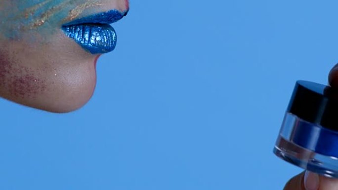 时装模特脸部下部的特写镜头。模特拿着蓝色眼影罐，亲吻它。时尚视频。