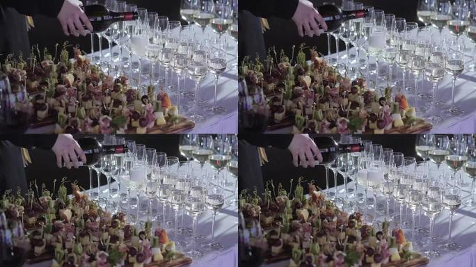 服务员把香槟倒进玻璃杯里.桌面装满了一杯起泡的白葡萄酒，背景是瓶子。