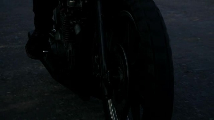 一个移动的摩托车前轮的特写视图。一个面目全非的人在乡村公路上骑着摩托车