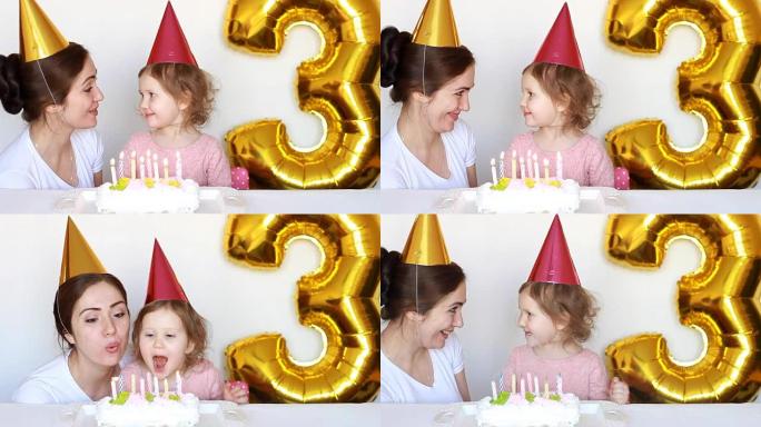 快乐的妈妈和孩子在聚会上吹灭生日蛋糕上的蜡烛。母亲，她的女儿微笑，笑着，在白色背景上拍手。3年。家庭