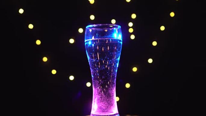 粉红色-蓝色灯光下的一杯水正在旋转。粉蓝色鸡尾酒。酒吧概念