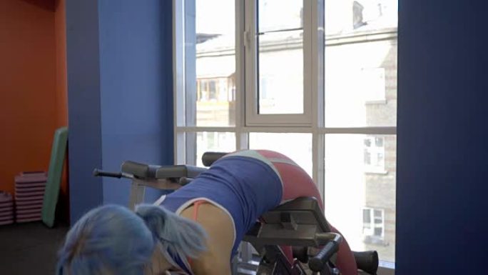 那个有着蓝色头发的女运动员在豪华的健身房的窗前梳理着她的后背