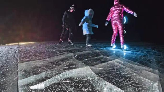 家庭正在滑冰之夜。女孩和男孩在大自然中骑花样冰鞋。母亲，父亲，女儿和儿子一起在裂缝中的冰上骑行。运动