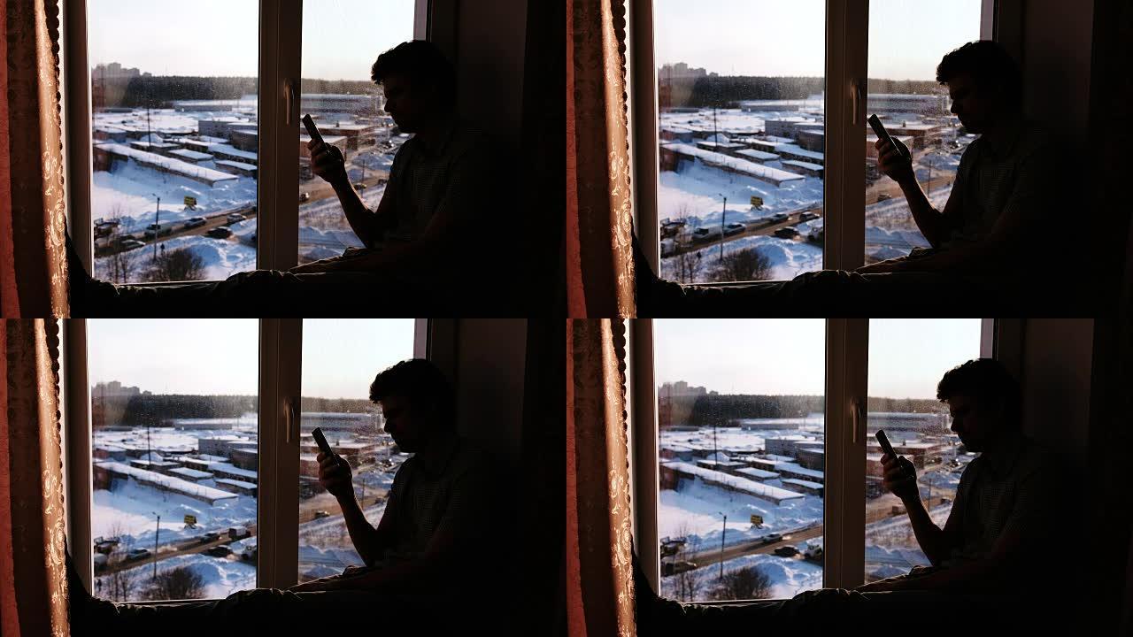 一个坐在窗台上的手机男人的剪影。