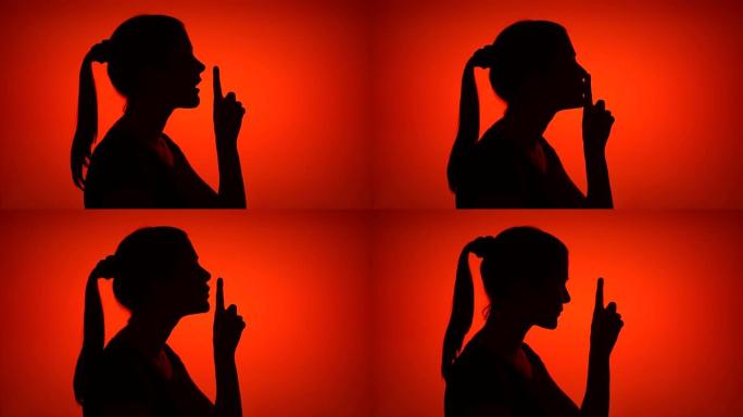 红色背景上年轻女子做沉默手势的剪影。神秘和保密的概念