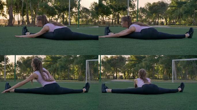 年轻漂亮的女人坐在公园的足球场上伸展，晨练，健身模型锻炼