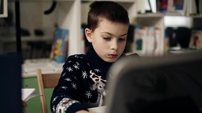 一个小男孩坐在笔记本电脑屏幕前的蓝色大眼睛肖像的慢动作镜头。编程类。教育过程。
