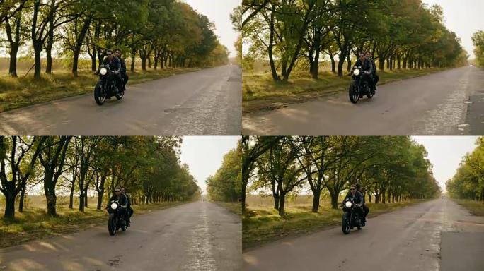 秋天在森林路上骑摩托车的年轻酷夫妇的跟踪镜头。戴着墨镜的迷人年轻人开着直升机，而他的女朋友坐在后面