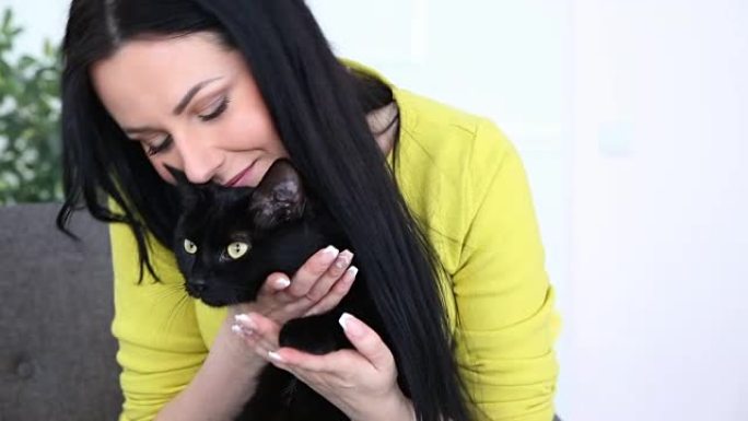 对宠物的爱。美丽的黑发女孩和一只黑猫正在沙发上的客厅里放松。