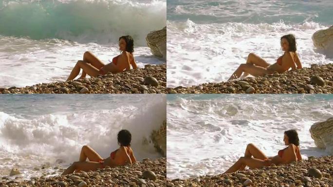 美丽的年轻女子坐在海岸上，看海浪很有趣