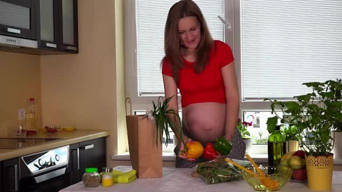 微笑的孕妇在厨房桌子上卸下装有有机食品的纸袋