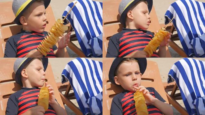 男孩在海边的棍子上吃自制的薯片。躺在躺椅上。