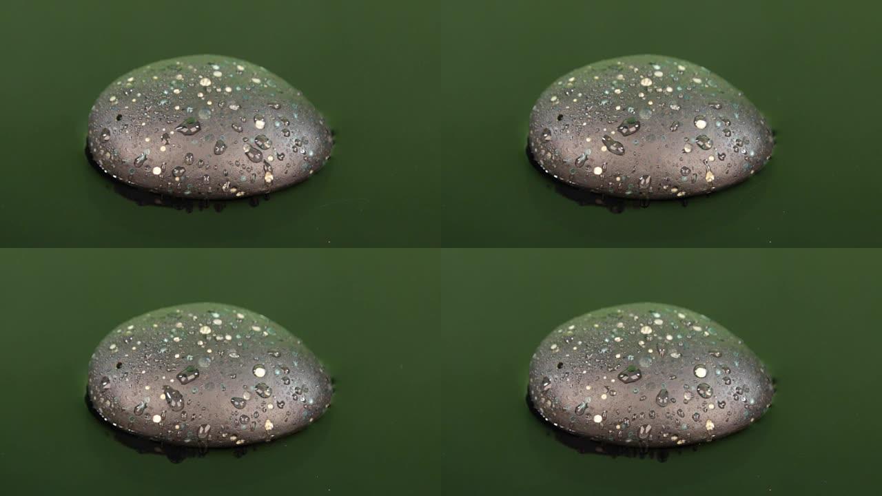 滴下一滴水在绿色水中的黑色石头上破裂