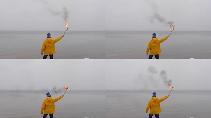 在冰冻的大海背景下，穿着黄色外套的火把的人的后视图。雪落在前景