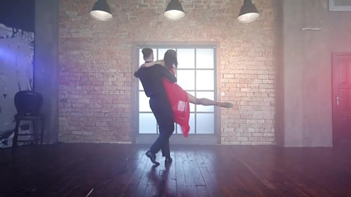 一对令人惊叹的夫妇在烟雾中的现代工作室里跳拉丁舞。